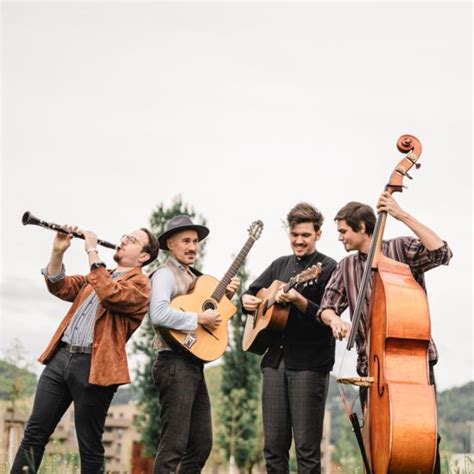 Vier Musiker spielen im Freien. Einer spielt Klarinette, zwei Gitarre und einer Kontrabass. Sie lachen und wirken fröhlich.